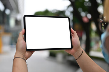 Close-up image of hand holding a white blank screen digital tablet over blur shopping center as a background.