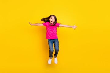 Poster - Photo of little girl jump hands wings plane pose flight wear pink t-shirt jeans sneakers isolated yellow color background