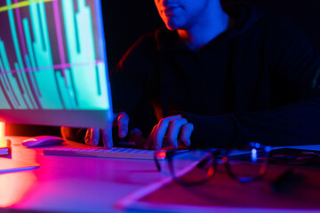 Cropped view of programmer using computer with charts reflection near eyeglasses on table on black background