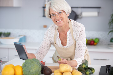 senior woman cooking with help of recipe on tablet