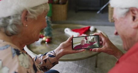 Canvas Print - Smiling senior caucasian couple using smartphone for christmas video call with man on screen