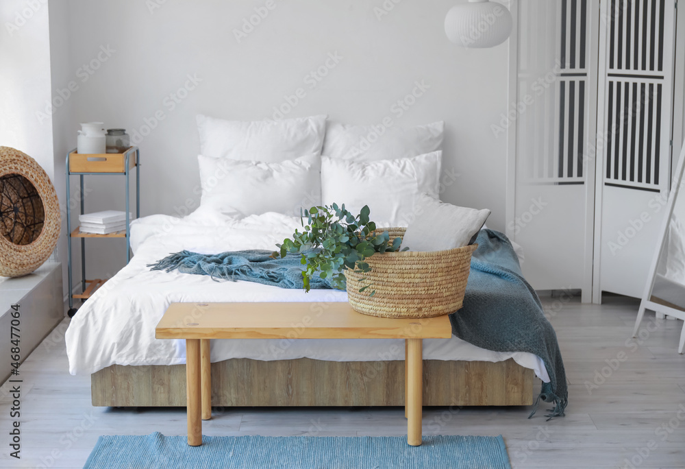 Basket with green eucalyptus branches on bench in bedroom