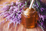 Fototapeta Lawenda - Heather honey in a glass jar and a bunch of forest heather flowers on a wooden table surface, soft selective focus. Alternative medicine