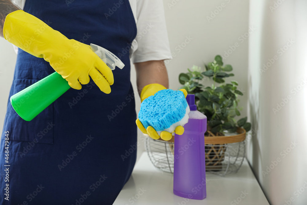 Young man spraying detergent onto cleaning sponge at home, closeup