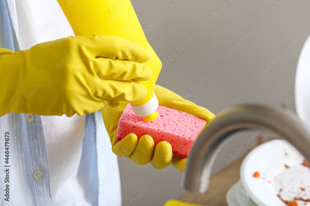 Young man pouring detergent onto sponge in kitchen, closeup