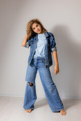 Wall Mural - young curly haired woman with blue eyes in a full length denim suit. model poses in the studio. space for text. High quality photo