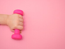 Children's Hand Holds A Kettlebell On A Pink Background. Place For Text.