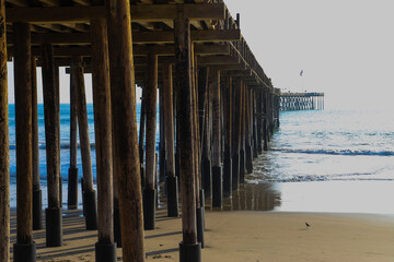 a shot of a long winding brown wooden pier at the beach with silky brown sand and vast blue ocean water with waves rolling in at Ventura Pier in Ventura California USA