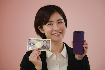 五千円札とスマートフォンを持つ女性