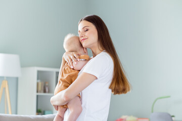 Poster - Profile side view portrait of attractive careful dreamy girl holding nursing embracing baby at light home flat indoors