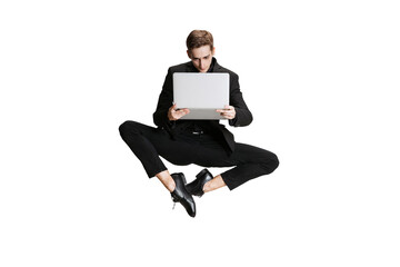 One handsome man in black business suit flying and using laptop isolated on white background. Art, inspiration concept.