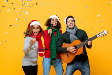  Group of Happy diverse close friends having party singing and celebrating Christmas in yellow studio background with confetti