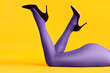 Legs of beautiful young woman wearing bright tights and high heels shoes lying on bright yellow background.