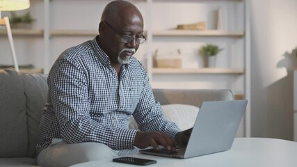 Serious elderly african american man freelancer in eyeglasses typing on laptop, working from home online, free space