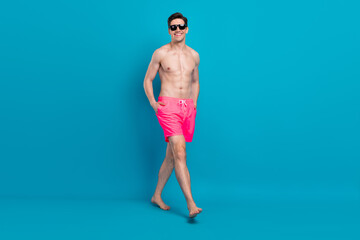 Wall Mural - Photo of cheerful positive young man naked torso dark eyewear walking arms hands pockets smiling isolated blue color background