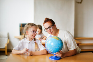 Wall Mural - a teacher and a girl, a student, a child at school at a desk working with a globe, a teacher and a student are studying geography, looking for countries on the map. , modern education and technology