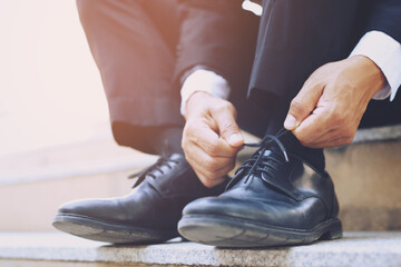  Close up of businessman hand tie shoelaces wearing leather shoes sitting on staircase background.