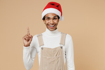 Wall Mural - Young african man 20s wear Santa Claus red Christmas hat holding index finger up with great new idea isolated on plain pastel beige background studio portrait. Happy New Year 2022 celebration concept.