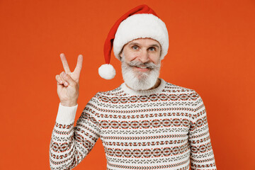 Wall Mural - Old happy bearded Santa Claus man 50s wear Christmas hat sweater posing showing victory sign isolated on plain orange background studio. Happy New Year 2022 celebration merry ho x-mas holiday concept