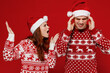 © ViDi Studio - Young angry swearing couple friends two man woman in sweater hat scream shout arguing isolated on plain red background studio portrait. Happy New Year 2022 celebration merry ho x-mas holiday concept.