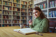 © Evgenii Starkov - Girl in library with book at desk looks with smile directly into camera.