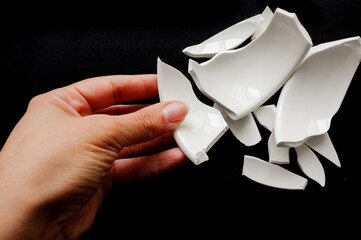 Woman hand assembling broken pottery on black background.