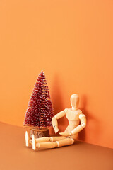 Wall Mural - Wooden mannequin miniature doll and Christmas tree on brown background. Minimalistic holiday concept