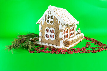 Homemade gingerbread house painted with white sweet icing and decorated with a pine branch on green screen background.