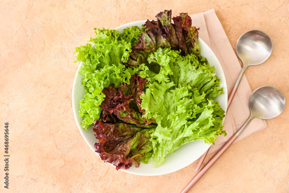 Bowl with fresh lettuce and spoons on color background