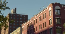 Flock Of Pigeons Flying In Sync From Roof Of Red Brick Apartment Building In New York City, U.S.A.