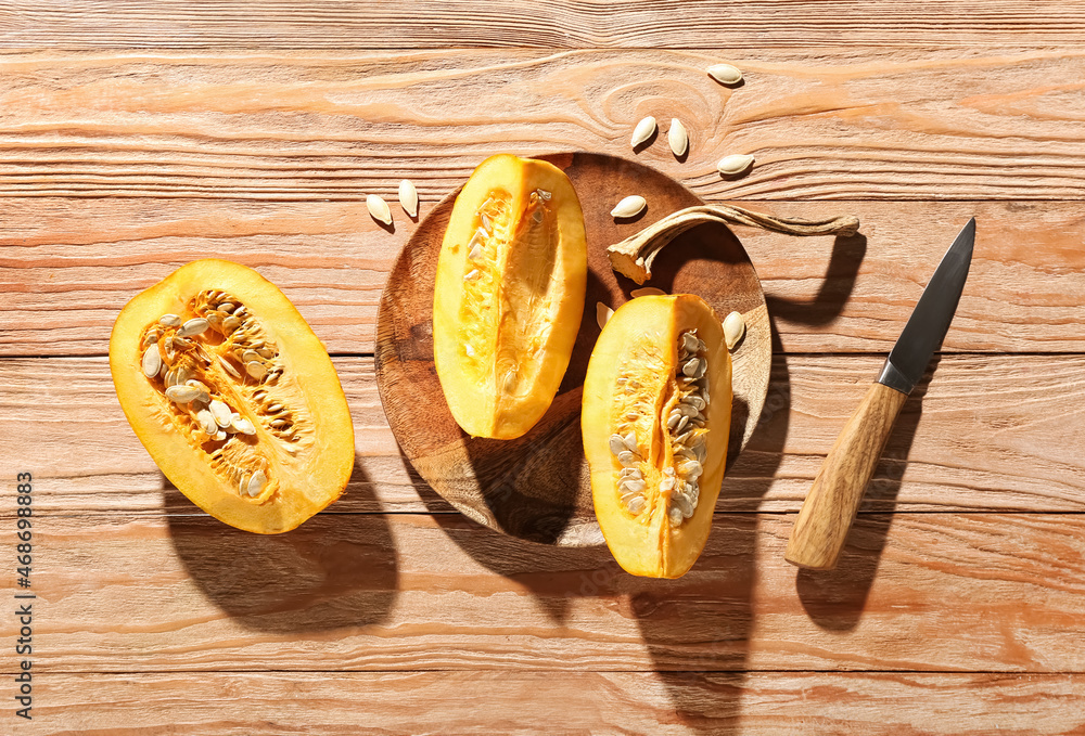Plate with cut pumpkin and knife on wooden background