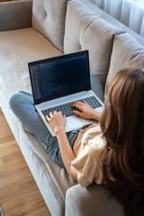 Wall Mural - Woman working on a laptop while sitting on the sofa. A girl programmer is coding