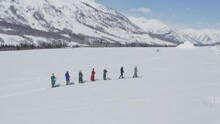 Aerial Shot Of A Group Of Tuva Men Dressed In Deel Walking In Skis In Snow Covered Steppe. Winter Day In Hemu Village, Xinjiang, China.