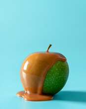 Caramel Apple Isolated On A Blue Background. Green Apple Covered In Caramel Sauce