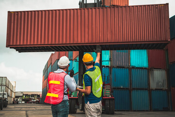 Industrial worker works with co-worker at overseas shipping container yard . Logistics supply chain management and international goods export concept .