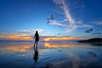 Poster - Sky and sea. Beautiful sunset. Silhouette of young woman walking on ocean beach.