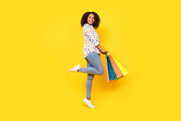 Full size profile photo of funny young wavy hairdo lady hold bags wear blouse jeans shoes isolated on yellow background