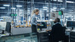 © Gorodenkoff - Car Factory Office: Female Supervisor Talks with Male Automotive Engineer, Using Computer to Design Advanced 3D Models for High-Tech Engines. Automated Robot Arm Assembly Line Manufacturing Vehicles