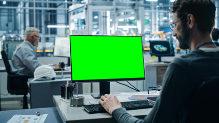 Poster - Car Factory Office: Caucasian Male Automotive Engineer Sitting at His Desk Working on Green Screen Chroma Key Computer. Automated Robot Arm Assembly Line Manufacturing. Over Shoulder Shot