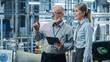 © Gorodenkoff - Car Factory: Female Project Manager Talks to Male Automotive Engineer, Plan Strategy Using Tablet Computer. Automated Robot Arm Assembly Line Production Conveyor Manufacturing Electric Vehicles