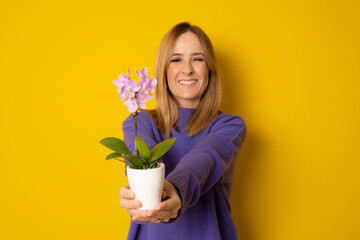 Happy young woman holding an orchid flower in a pot isolated on yellow background