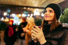 Close-up Of Young Beautiful Girl In Winter Attire Drinking Hot Drinks And Dreaming. Spending Time With Friends At Winter Fair At Evening.