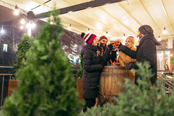 Wall Mural - Young happy people, friends with glasses of beer and sausages having fun, spending time together at winter fair at evening. Holidays, Christmas concept