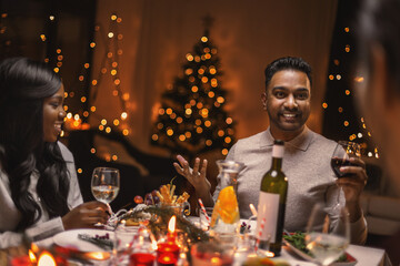 Wall Mural - holidays, party and celebration concept - multiethnic group of happy friends having christmas dinner at home and drinking wine