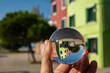 Hand holding glass sphere in front of colorful houses