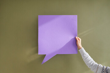 Anonymous adult showing one purple square shaped mockup copyspace speech bubble in hand on greyish green background. Free, blank, clean violet paper for expressing opinion and getting message across