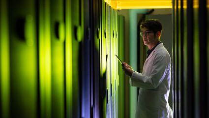 Asian male engineer wearing an apron using digital tablet while inspecting in computer server room