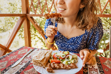 Wall Mural - A woman eats an Armenian dish Lula Kebab with lavash in a cafe