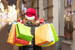 © Наталья Жукова - girl in a red santa claus hat with gifts in hands on the street of the city. Christmas mood