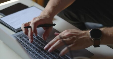 Close-up of hands with pen of unrecognizable businessman typing on laptop computer at the desk. Concept of remote home working, distance education. Shooting in slow motion.